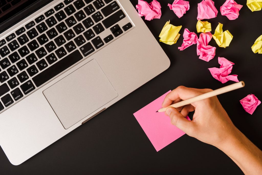 A hand writing on a notepad, with a laptop displaying a blog post, symbolizing content creation for guest posts.