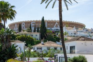 Large circular arena building behind white Mediterranean-style homes and palm trees