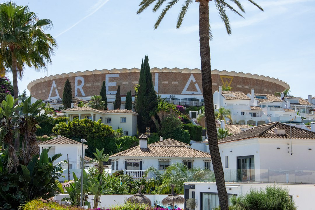 Large circular arena building behind white Mediterranean-style homes and palm trees